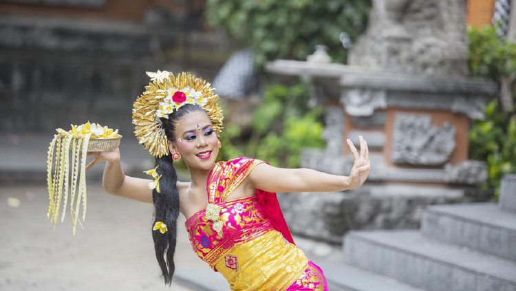 Beautiful female dancer carrying a bowl of flower petals while performing Pendet dance in the temple