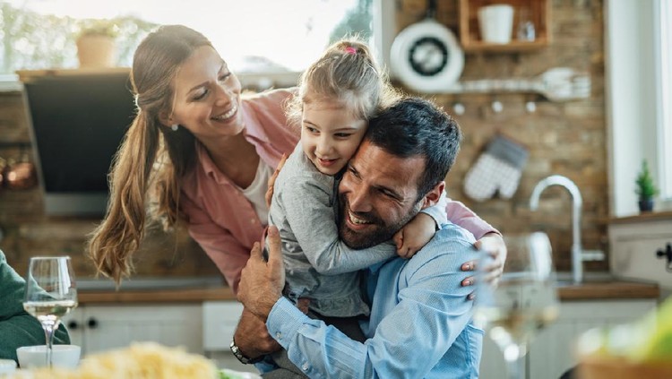Young happy parents embracing with their small daughter during lunch at dining table.