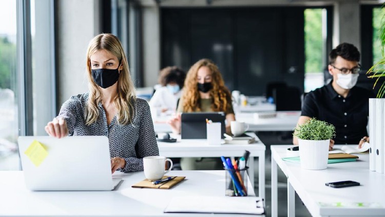 Young people with face masks back at work in office after coronavirus quarantine and lockdown.