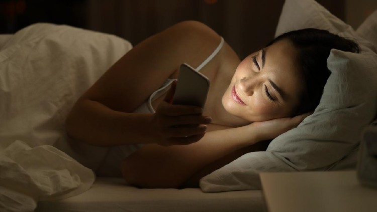 Relaxed girl using a smart phone lying on the bed in the night