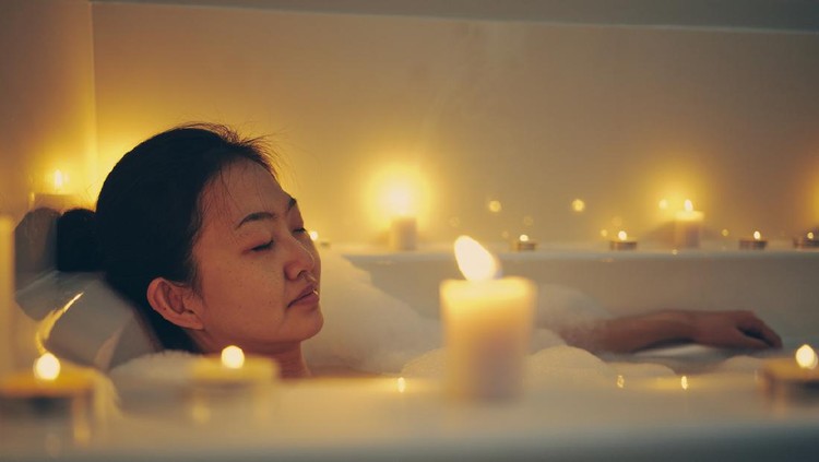 A young Japanese woman relaxing in a bathtub, surrounded by candles.