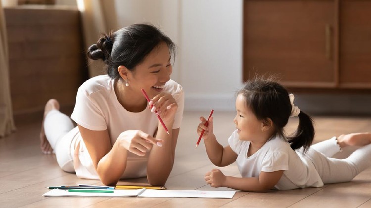 Ilustrasi Bermain dengan Anak Educational pastime develop creativity skill in kid concept. Asian mother her small daughter lying on warm wooden floor in sunny cozy living room, mom teach girl paint use album and colourful pencils