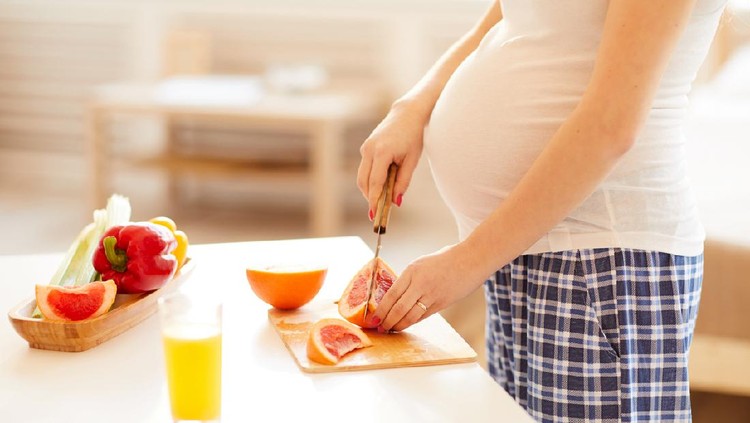 Side view of unrecognizable pregnant woman cutting oranges for healthy breakfast in morning, copy space