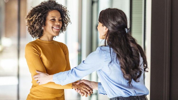 Two Successful businesswomen are shaking hands. They are standing near the office and smiling. They made a deal