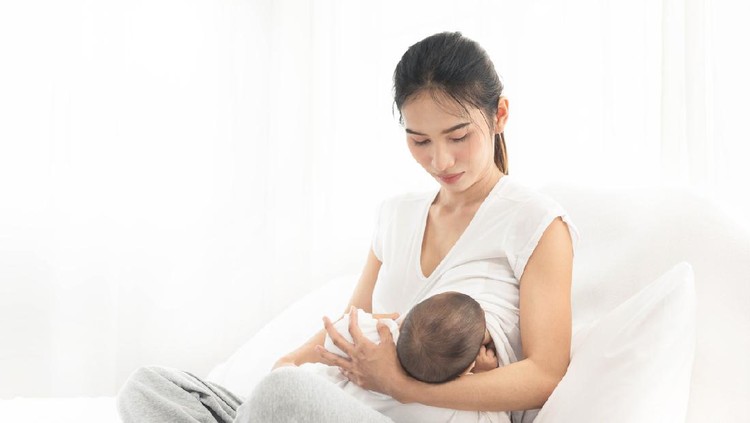 Young asian mother feeding breast her baby on bed at home in white room. Asia mom holding her baby and looking to her child.  Woman and new born relax in a white bedroom.