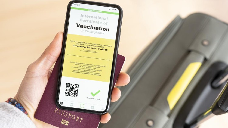 (Selective focus) Overhead view of an human hand holding a passport and a smart phone with a digital illustration of an example of a certificate of vaccination against the Covid-19 disease.