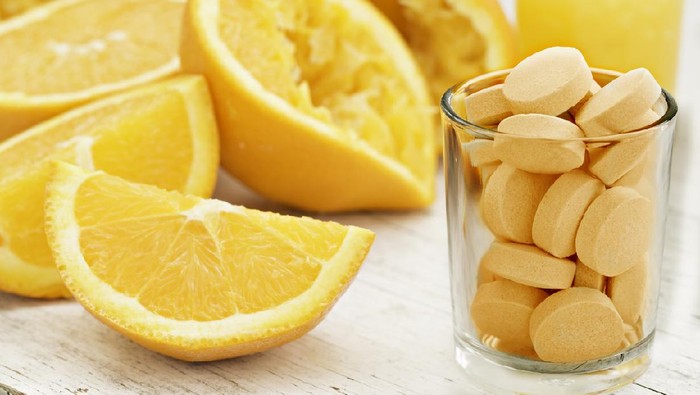 A close up shot of sliced and squeezed oranges a glass of orange juice and a glass full of orange flavored vitamin C Pills. Eat the orange, drink the juice or take a pill.
