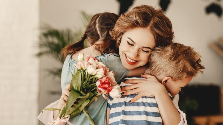 Happy Mothers Day! Children boy and girl congratulate smiling mother, hugs her  and give her flowers   bouquet of tulips during holiday celebration in kitchen at home