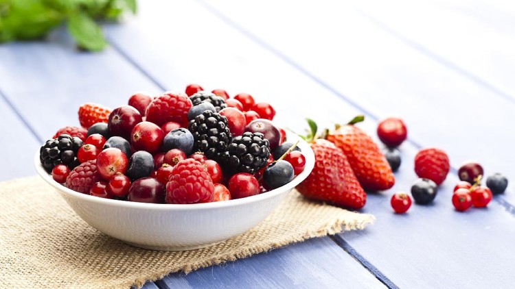 White bowl filled with fresh mixed organic berries on blue garden table. Some berries are scattered outside the bowl. DSRL studio photo taken with Canon EOS 5D Mk II and Canon EF 100mm f/2.8L Macro IS USM