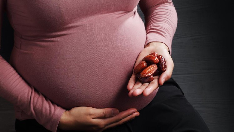Pregnant woman holding dried Date Palm fruit on black background