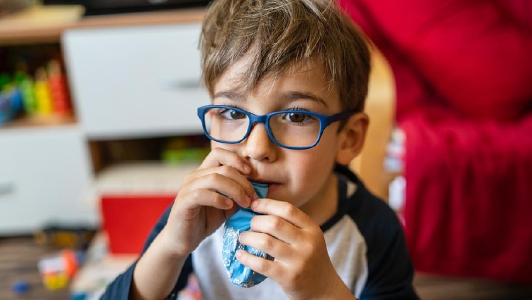 Portrait of happy caucasian boy with eyeglasses sitting at home in room in day real people small male playful child playing on the floor inflating balloon
