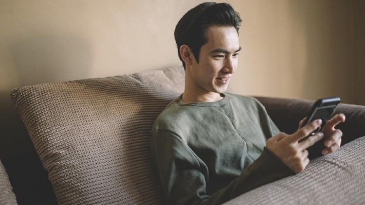 Ilustrasi Main Sosial Media an asian chinese man sitting on his sofa with cushion relaxing with his smart phone surfing the net and shopping online