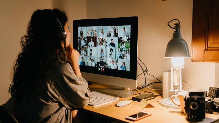 Young woman having a video call with her colleagues during Covid-19 Coronavirus quarantine. Many people on the screen.
