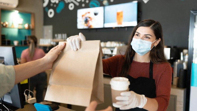 Young female staff giving parcel and coffee to customer at takeaway counter in coffee shop