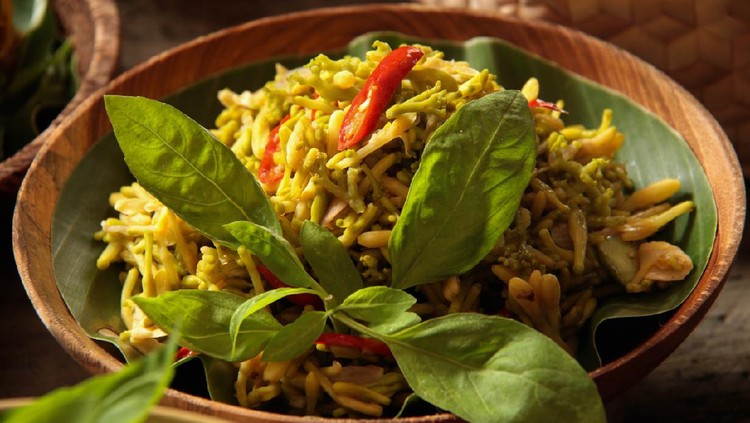 Garo Bunga Pepaya, the traditional Minahasan dish of sautéed papaya flower buds. The dish is plated on a shallow wooden bowl lined with banana leaf and garnished with basil leaves.