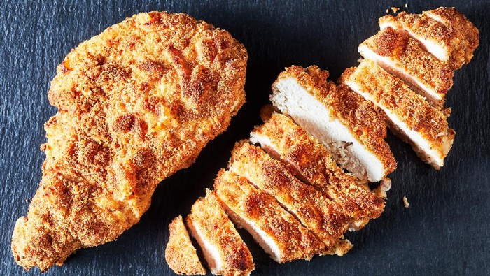 fried breaded chicken breasts, a whole one and a sliced one on a black stone plate, horizontal view from above