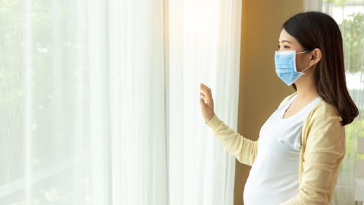 Worried pregnant woman with protective face mask on sofa at home. sick pregnant woman during COVID-19.