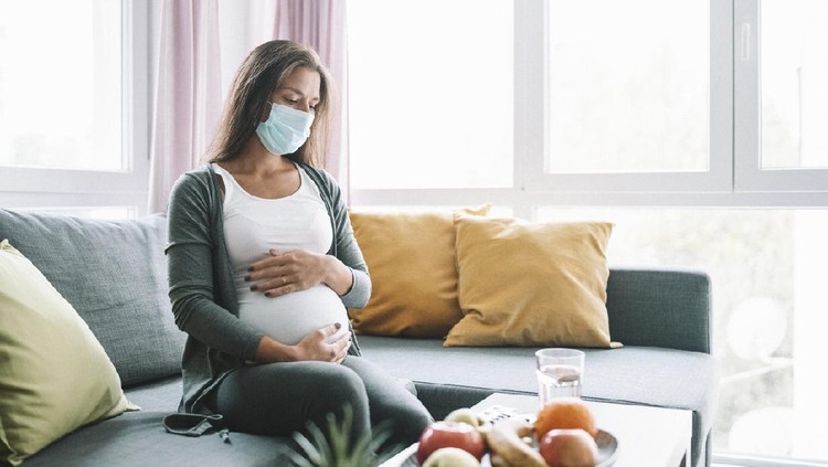 Worried pregnant woman with protective face mask on sofa at home. sick pregnant woman during COVID-19.