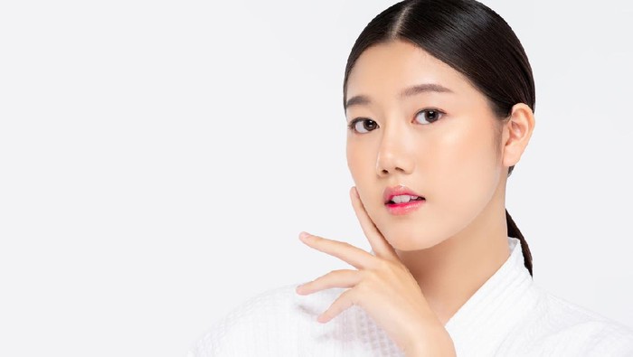 Youthful pretty Asian woman with hands touching face isolated on white background for beauty and skincare concepts