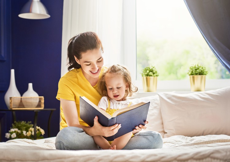 Pretty young mother reading a book to her daughter. Family holiday and togetherness.