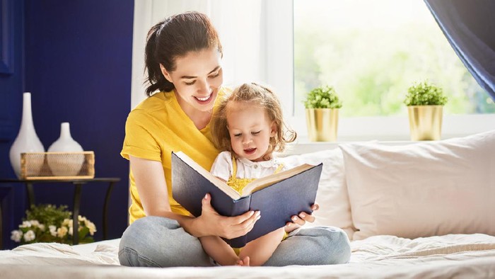 Pretty young mother reading a book to her daughter. Family holiday and togetherness.