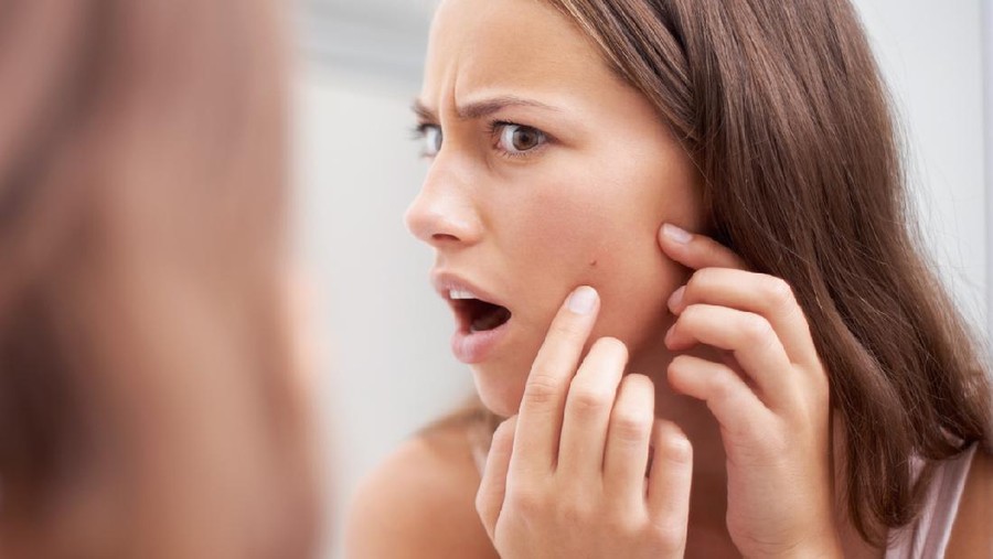 A young woman looking shocked as she examines her skin