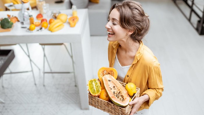 Portrait of a young and cheerful woman with exotic fruits at home. Concept of wellbeing, healthy food and homeliness