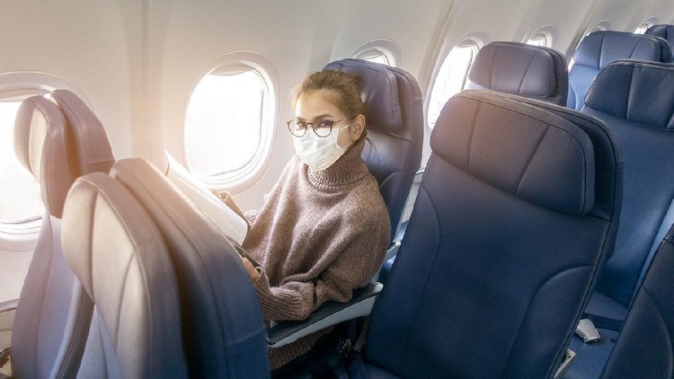 Ilustrasi perempuan di pesawat A young woman wearing face mask is traveling on airplane , New normal travel after covid-19 pandemic concept