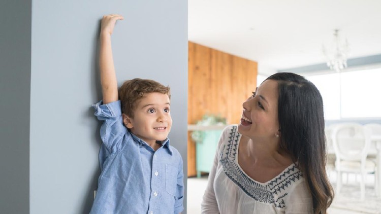 Happy mother measuring her son against the wall at home - parenting concepts