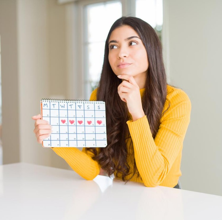 Young woman holding menstruation calendar serious face thinking about question, very confused idea