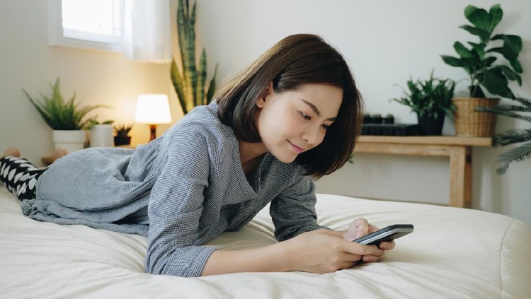 Young Asian woman using smart phone in bedroom happy and smile.