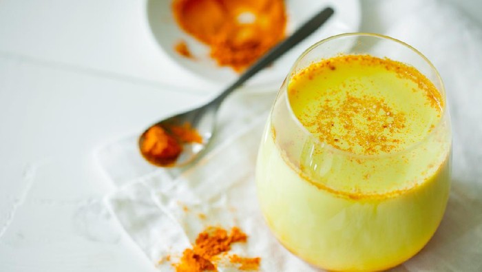 Healthy ayurvedic drink golden almond milk or pumpkin turmeric latte with curcuma powder on white background close-up. Trendy Asian natural detox morning beverage with spices for vegans. Horizontal orientation
