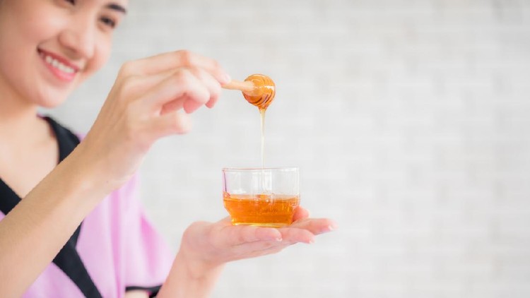 Beautiful asian young woman professional masseuse holding honey cup for spa body treatment in spa salon. Female masseuse prepared pure honey for facial mask. Beauty treatment and healthcare concept.