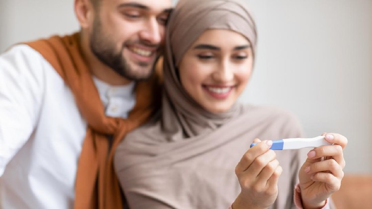 Awaiting Baby. Joyful Muslim Couple Holding Positive Pregnancy Test Sitting Together On Sofa Indoors, Focus On Test. Happy Parents-To-Be, Childbirth Concept. Shallow Depth, Cropped