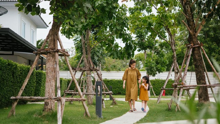 Two women waving good bye on the front lawn of a residential home.  The woman leaving is wearing protective gloves and a face mask.  They are practicing social distancing.