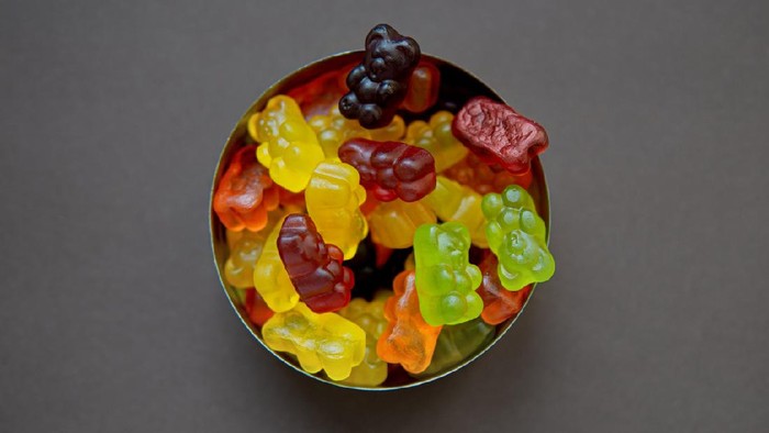 Top view on a round metal candy box full of gummy bears of different colors on a neutral background.
