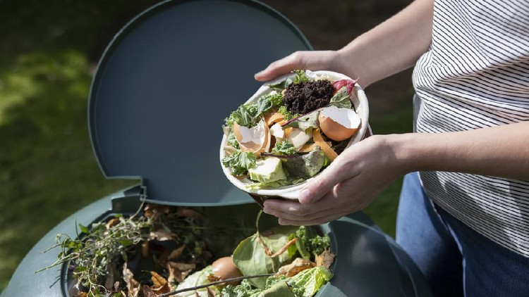 Close Up Of Woman Emptying Food Waste Into Garden Composter At Home