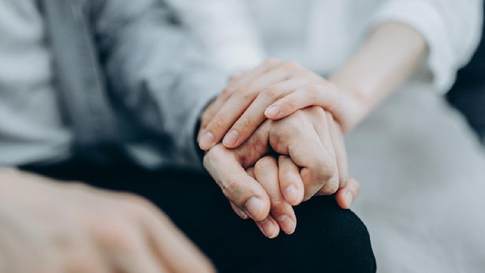 Cropped shot of a young couple sitting on sofa compassionately holding hands in self isolation during Covid-19 health crisis