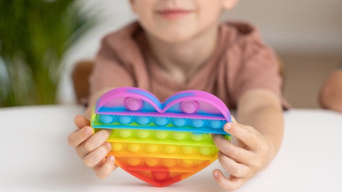 Cute child playing with the Pop It fidget. New anti stress game - push pop bubble flexible fidget. Sensory toy for discharge, development of kid