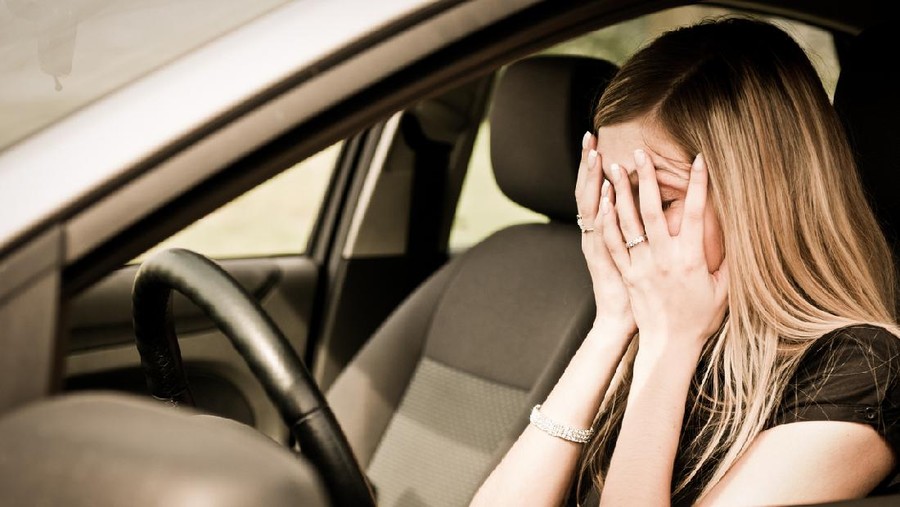 Young woman with hands on eyes sitting depressed in car