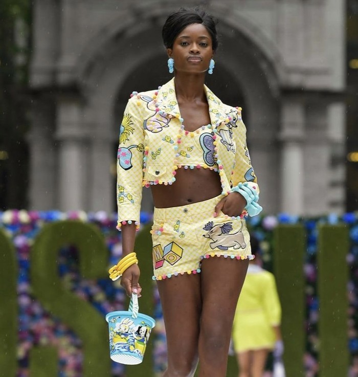 Kesan witty juga ditunjukkan pada setelan bra top, cropped blazer, dan shorts berwarna kuning pastel dengan gambar kartun. Foto: instagram.com/moschino