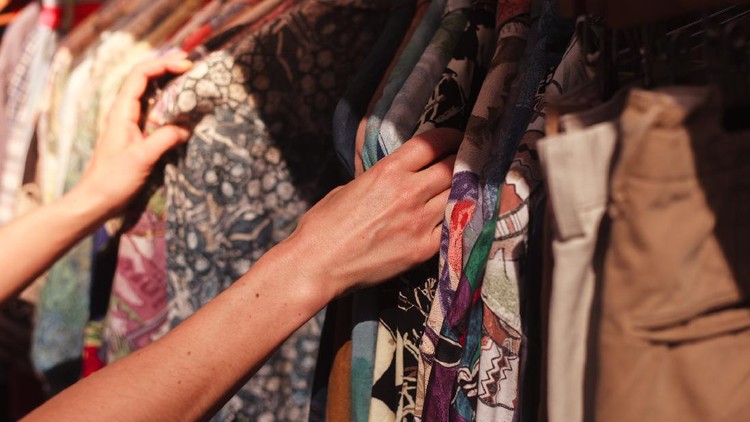 A young woman is browsing a rail of clothes at a street market