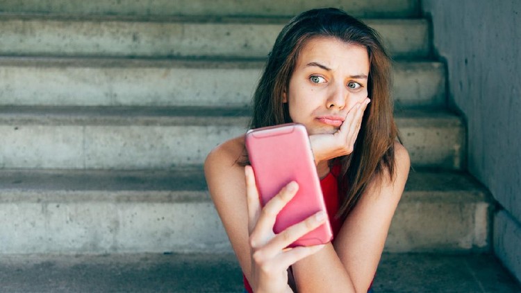 Displeased teen girl looking at her smartphone sitting on the stairs outdoors
