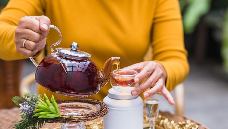 Woman pouring tea from glass pot into cup, Tea ceremony concept