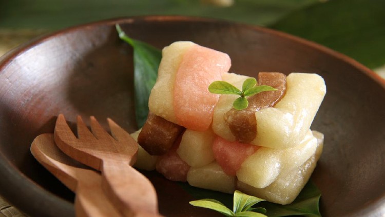 Getuk Tiga Warna or three-color getuk is the signature Javanese snack of mashed cassava and grated coconut cake from Magelang, Central Java, Indonesia. This cassava cake is always made and served in three flavors and colors. The cake is plated on an earthenware plate and garnished with a bunch of tiny leaves. A pair of wooden cutlery is placed on the plate.