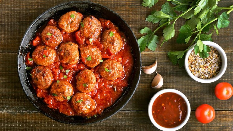 Bakso pedas Meatballs in cast iron pan, fresh parsley and tomatoes on wooden table, top view