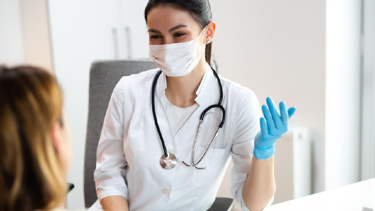 Caucasian doctor in medical mask speaking with mother about scoliosis of her daughter stock photo. Pediatrics concept