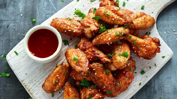 Baked chicken wings with sesame seeds and sweet chili sauce on white wooden board