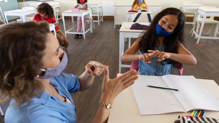 Caucasian female teacher wearing face mask at school, teaching children at school classroom. Education back to school health safety during Covid19 Coronavirus pandemic.