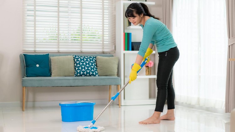 Attractive young Asian woman mopping tile floor at living room while doing cleaning at home during Staying at home using free time about their daily housekeeping routine.